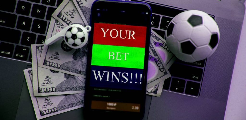 Smartphone with online gambling application, dollar bills and soccer ball on a keyboard